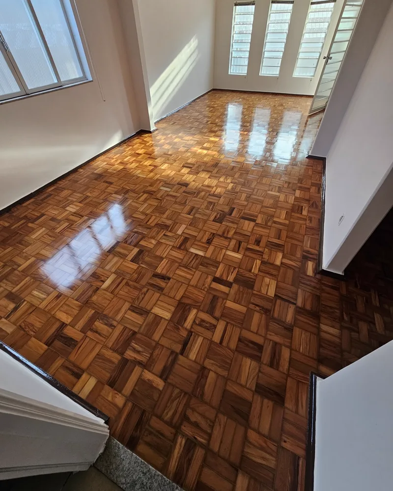 Sala com taco damero restaurado e acabamento sinteko em alto brilho, refletindo as janelas