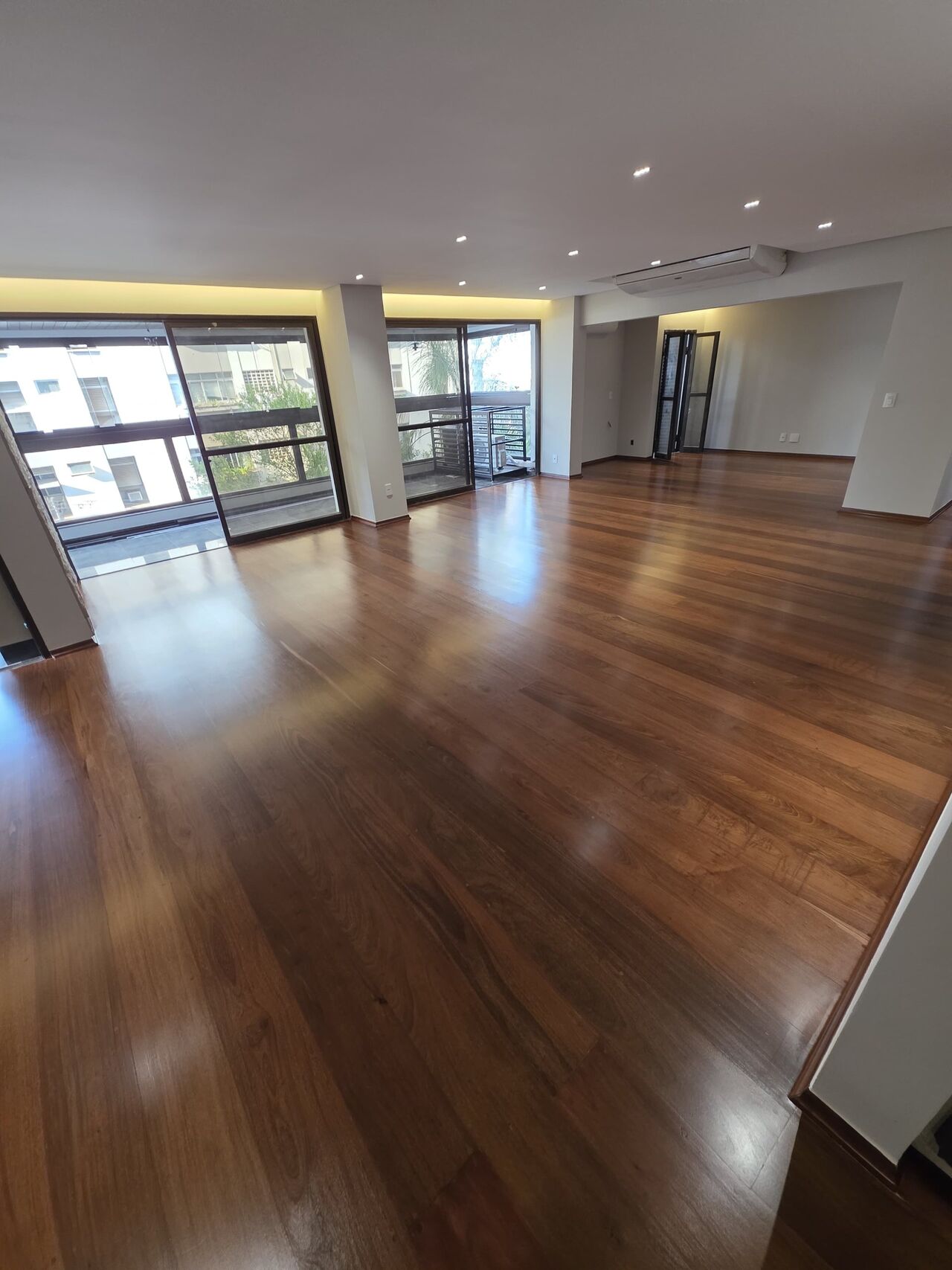 Sala ampla de alto padrão com assoalho de madeira restaurado, refletindo a luz das janelas