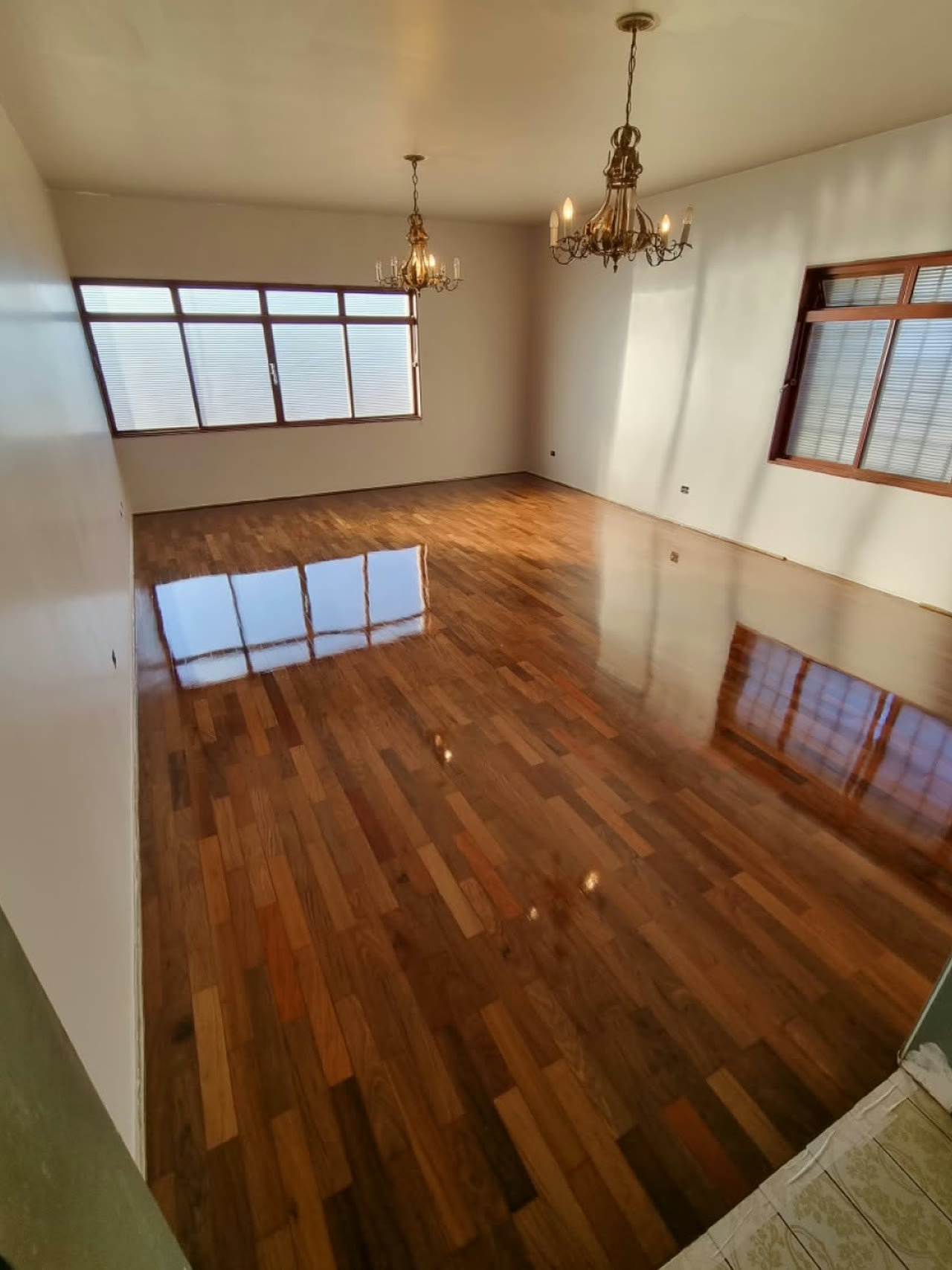 A mesma sala com o taco de ipê restaurado e brilhante, refletindo as janelas