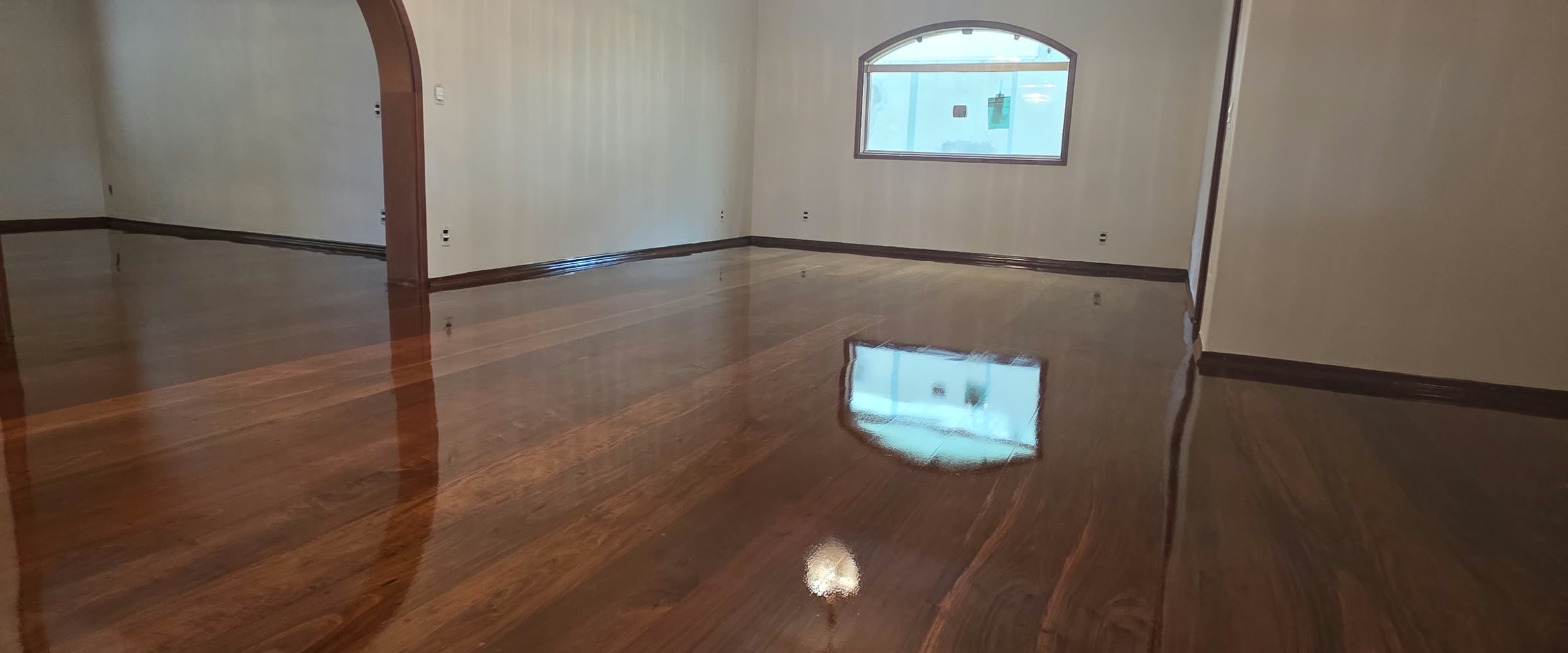 Sala com assoalho de tábua corrida restaurado em alto brilho, refletindo a janela em arco