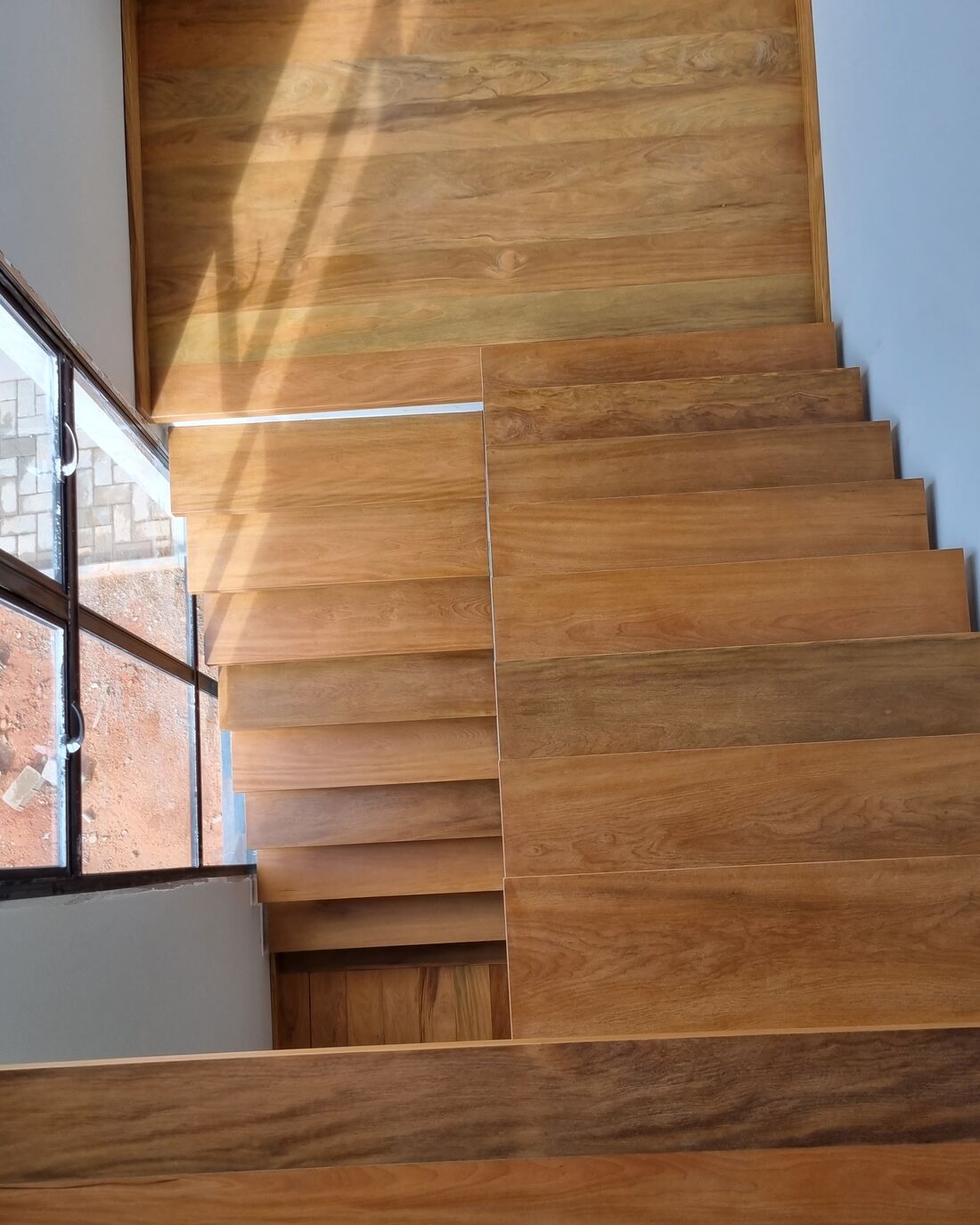 Escada de madeira maciça em obra, degraus largos com luz lateral
