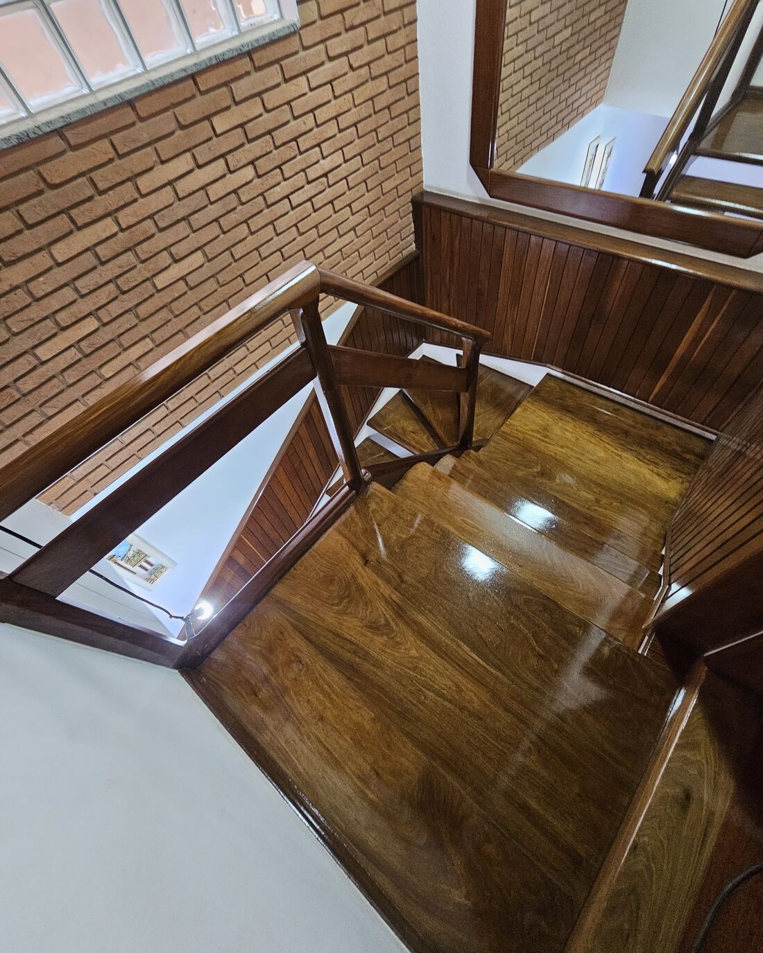 Escada em L com degraus e corrimão de madeira envernizados em alto brilho