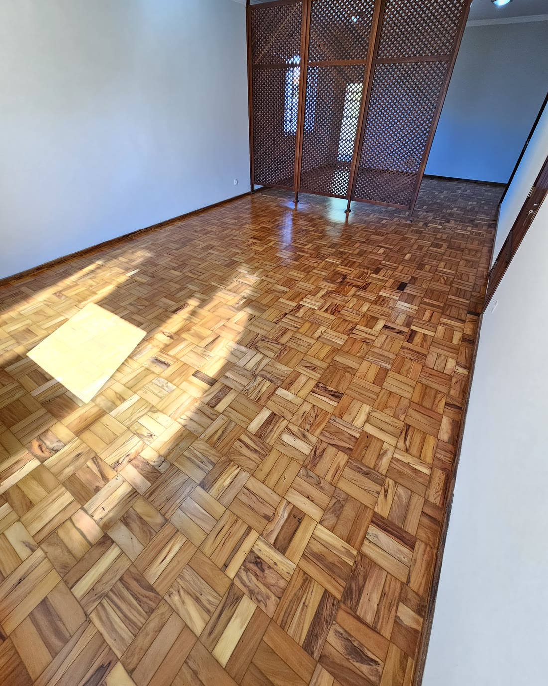 Sala com taco restaurado e envernizado, com a luz do sol entrando pela janela