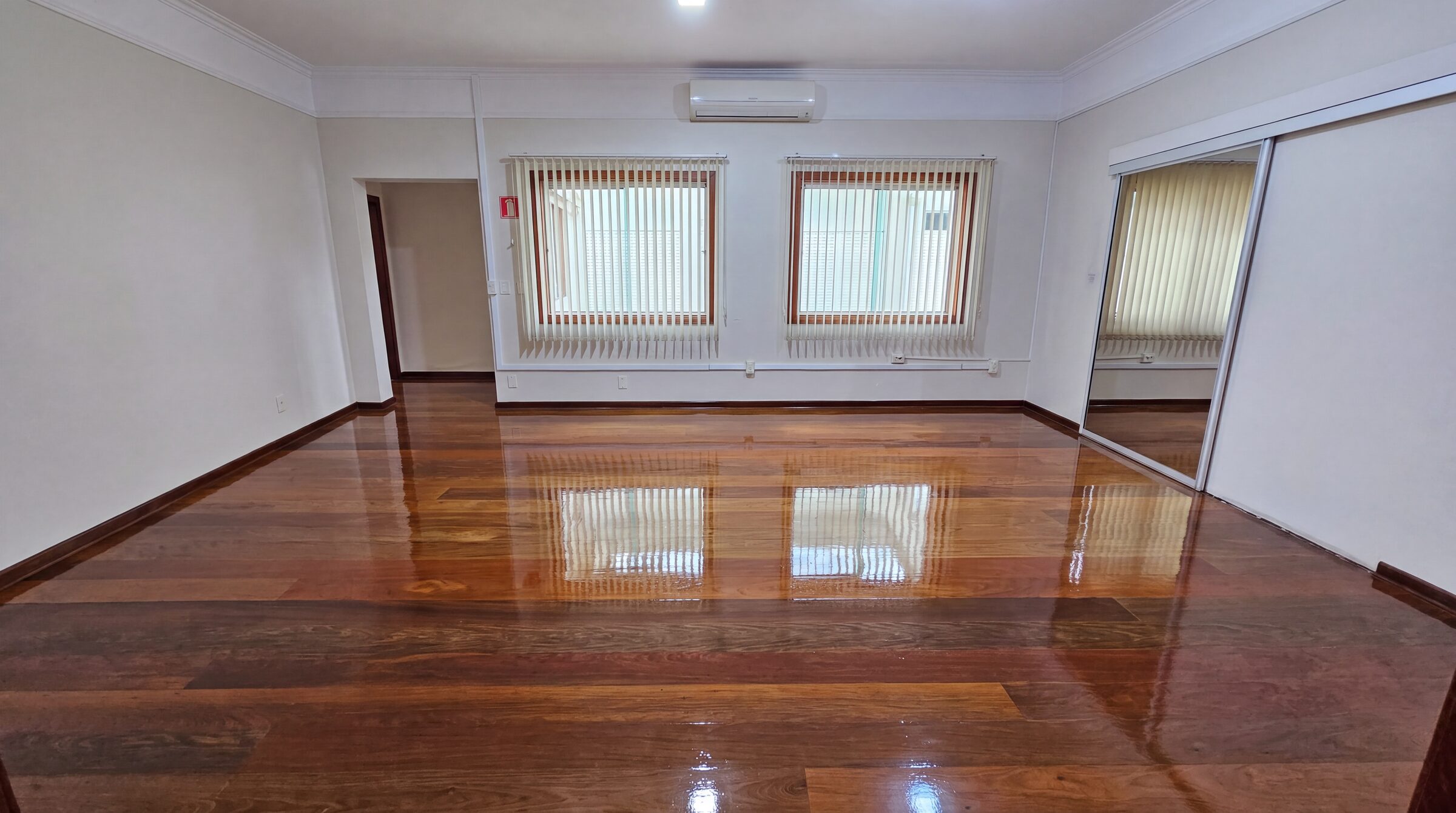 Sala ampla com piso de madeira restaurado, reflexo das janelas no verniz