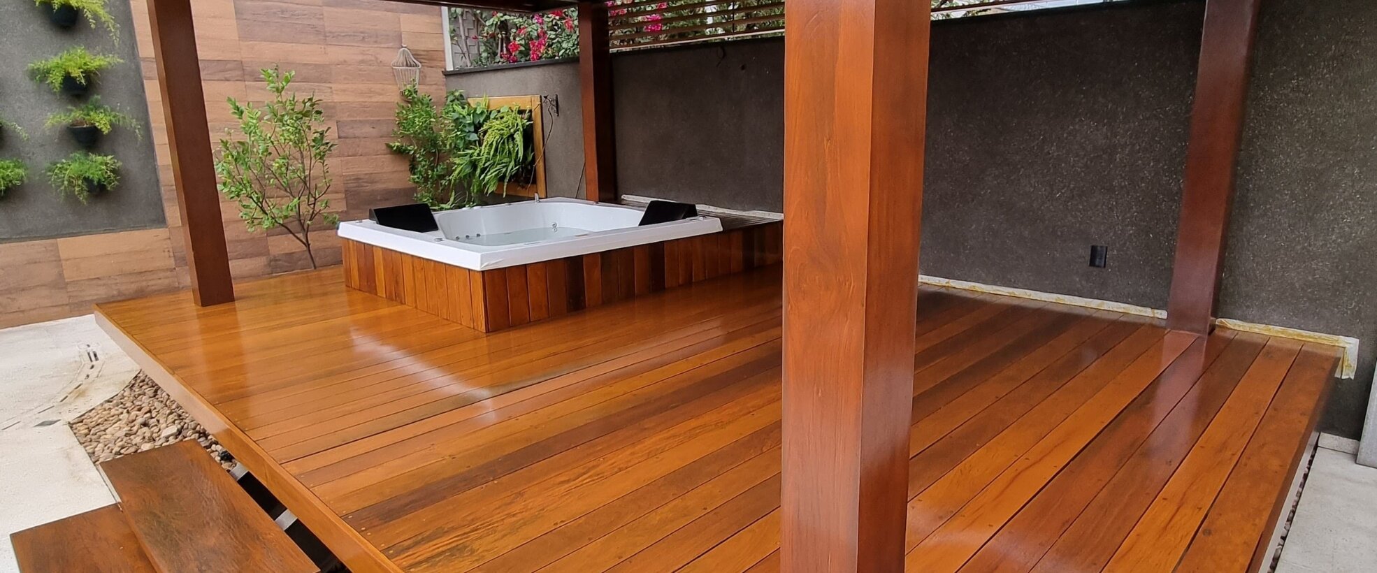 Deck de madeira restaurado sob pergolado, com spa e jardim vertical