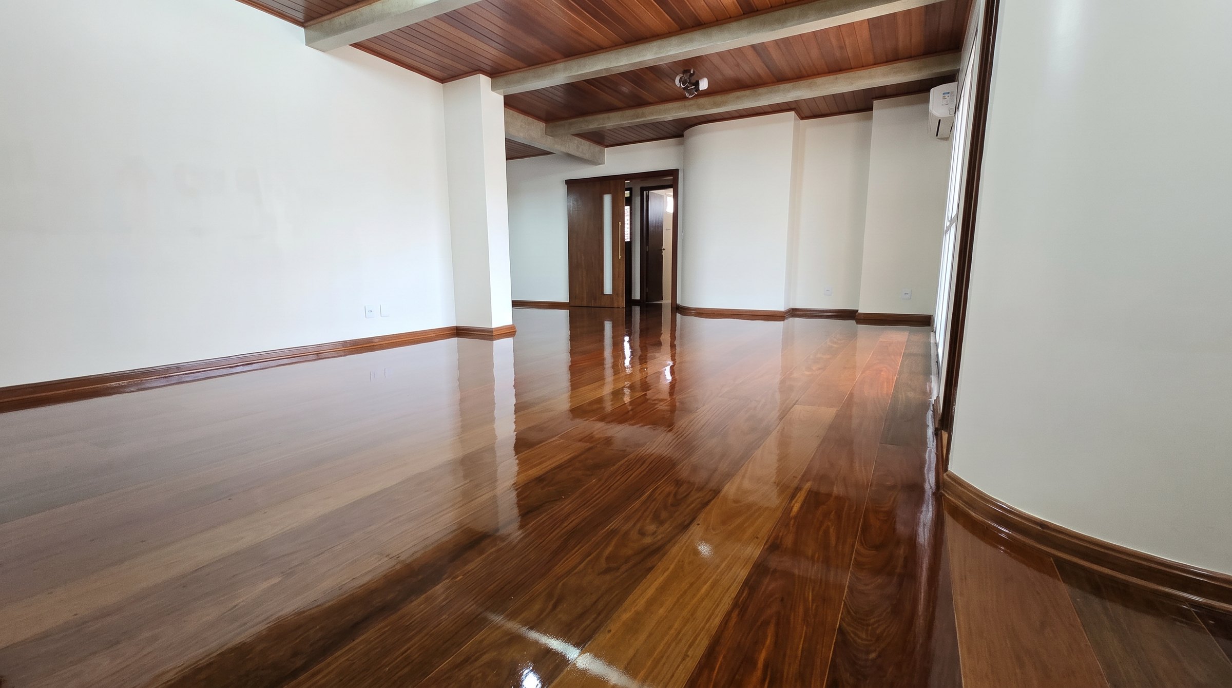Sala com piso de tábuas de madeira escura em alto brilho e forro de madeira