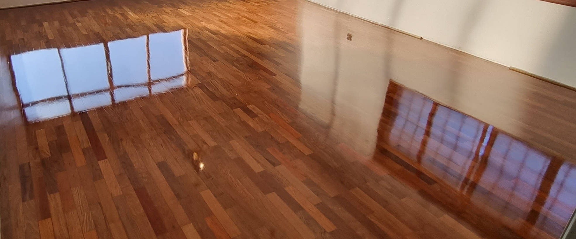 Sala com piso de tábuas de madeira restaurado em alto brilho, com reflexo das janelas