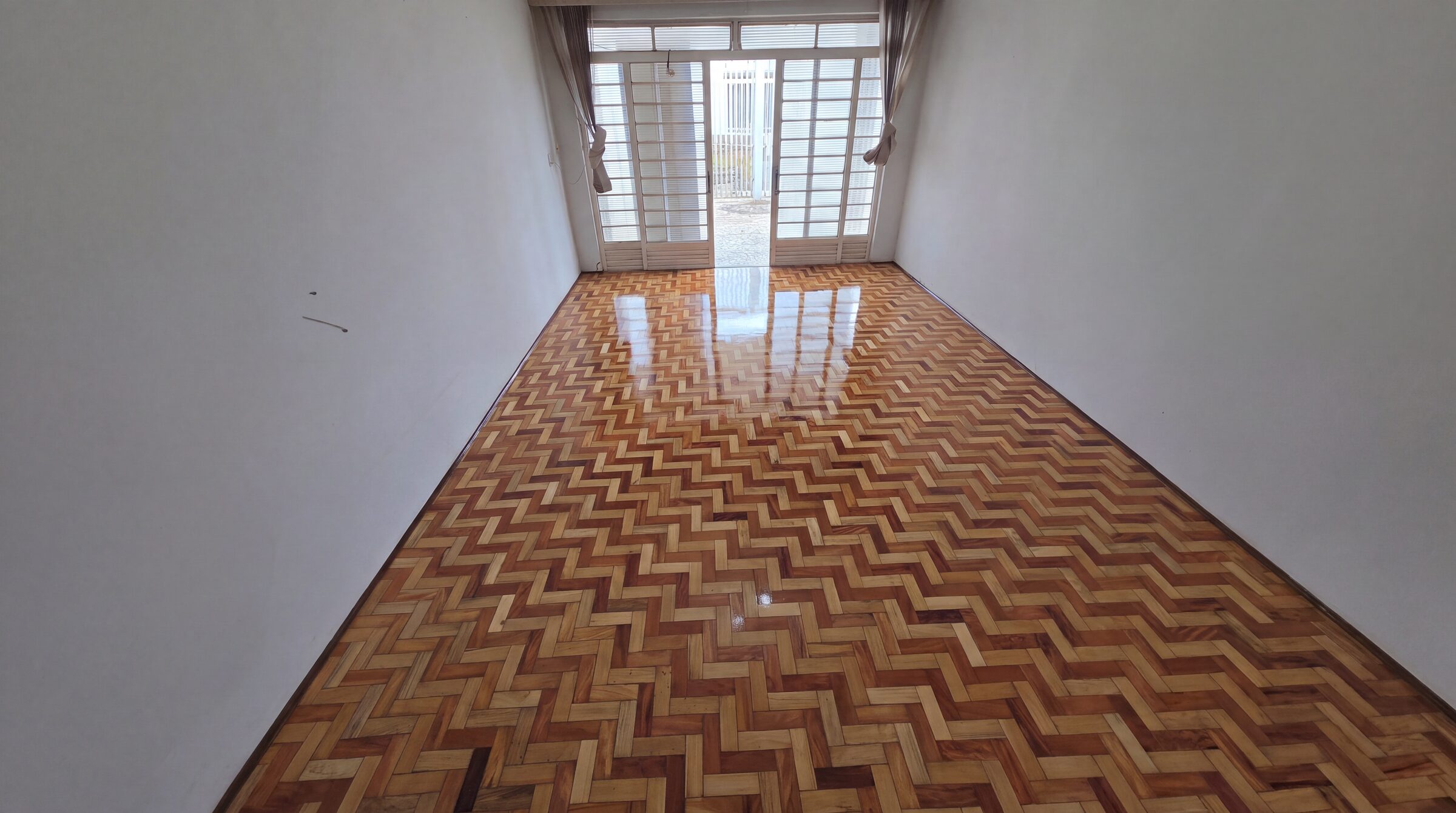 Sala com taco em espinha de peixe restaurado e envernizado, brilho uniforme e luz da porta-balcão